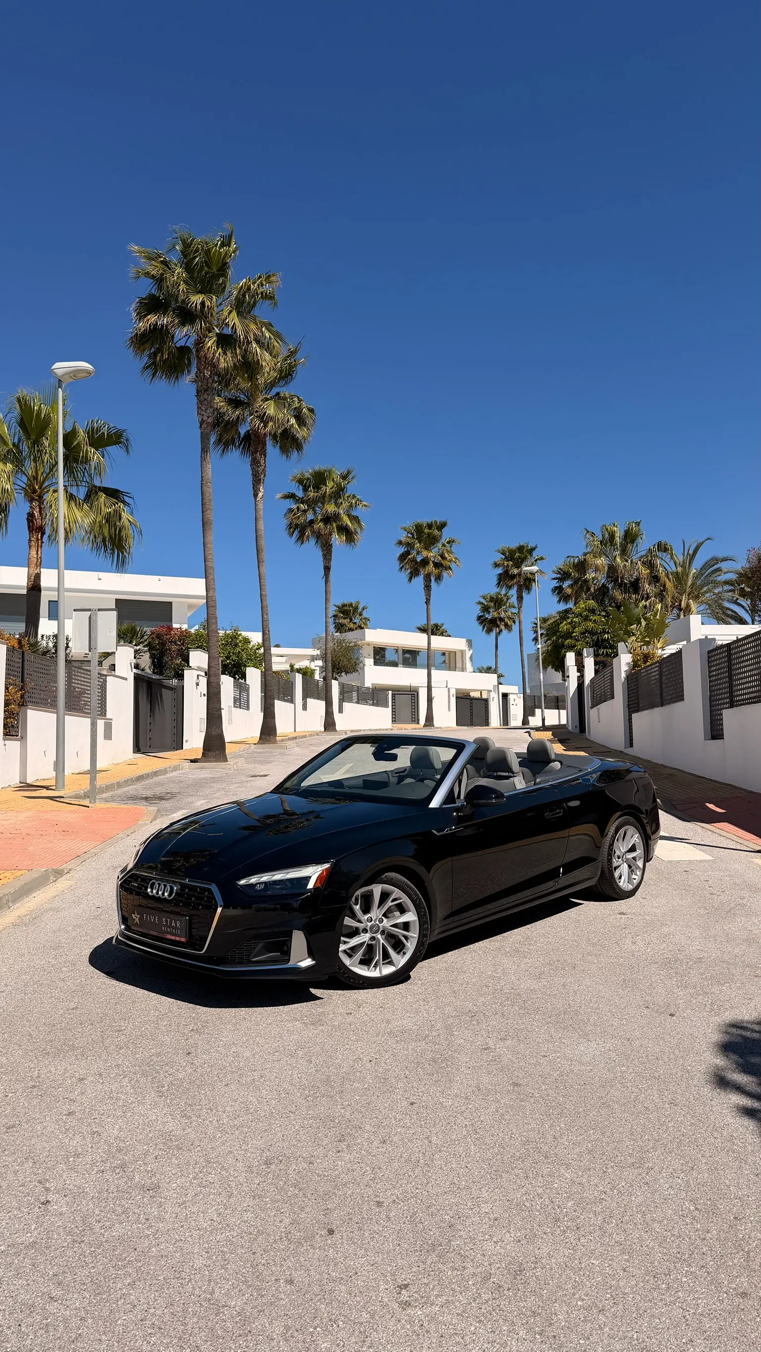 Audi A5 Convertible 45 TFSI Quattro in Mythos Black with top down, front three-quarter view with Five Star Rentals plate in a Marbella residential street