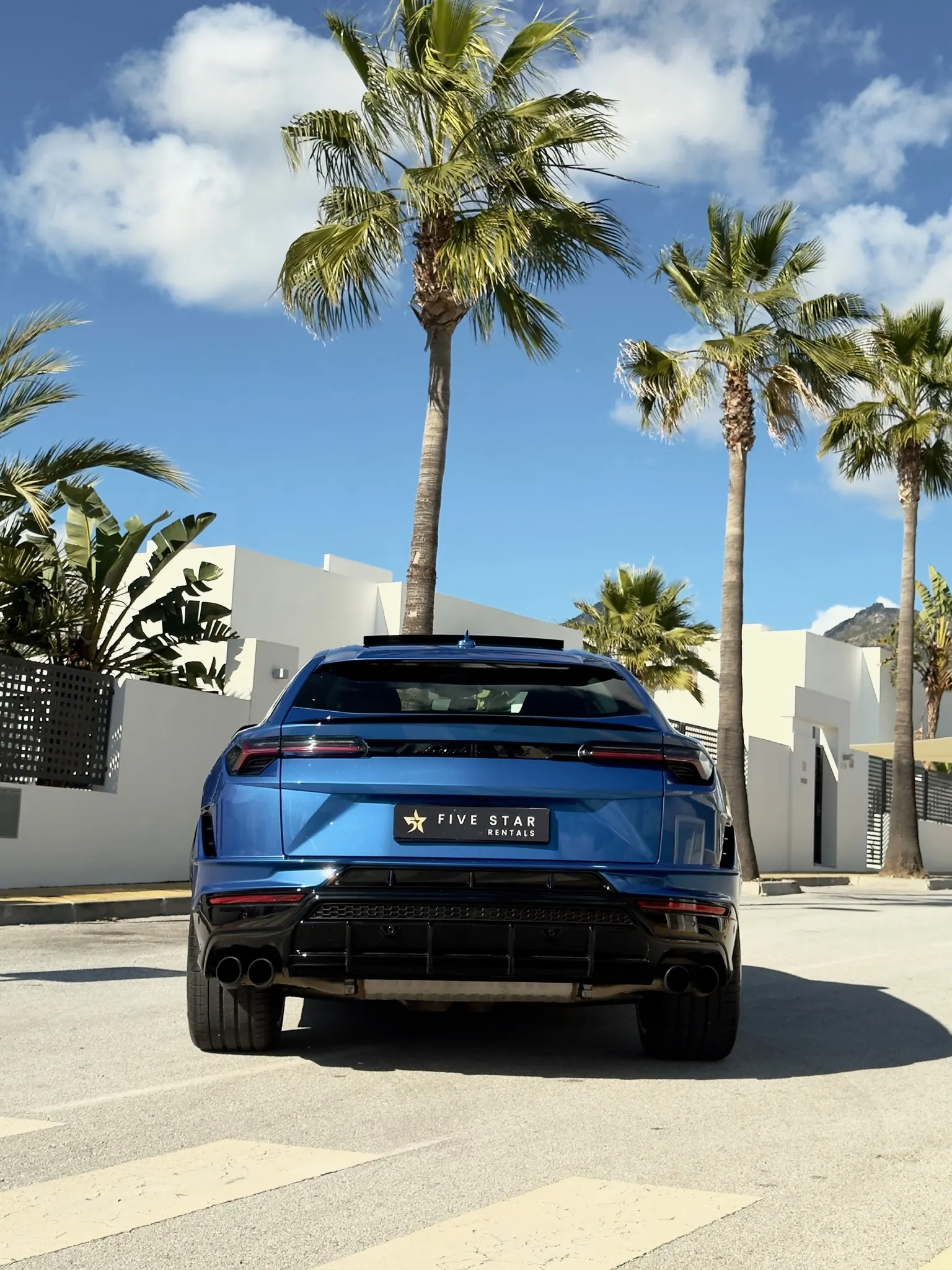 Centered rear view of the Blu Eleos Lamborghini Urus S with cursive Lamborghini badge, oval dual exhaust and Five Star Rentals plate