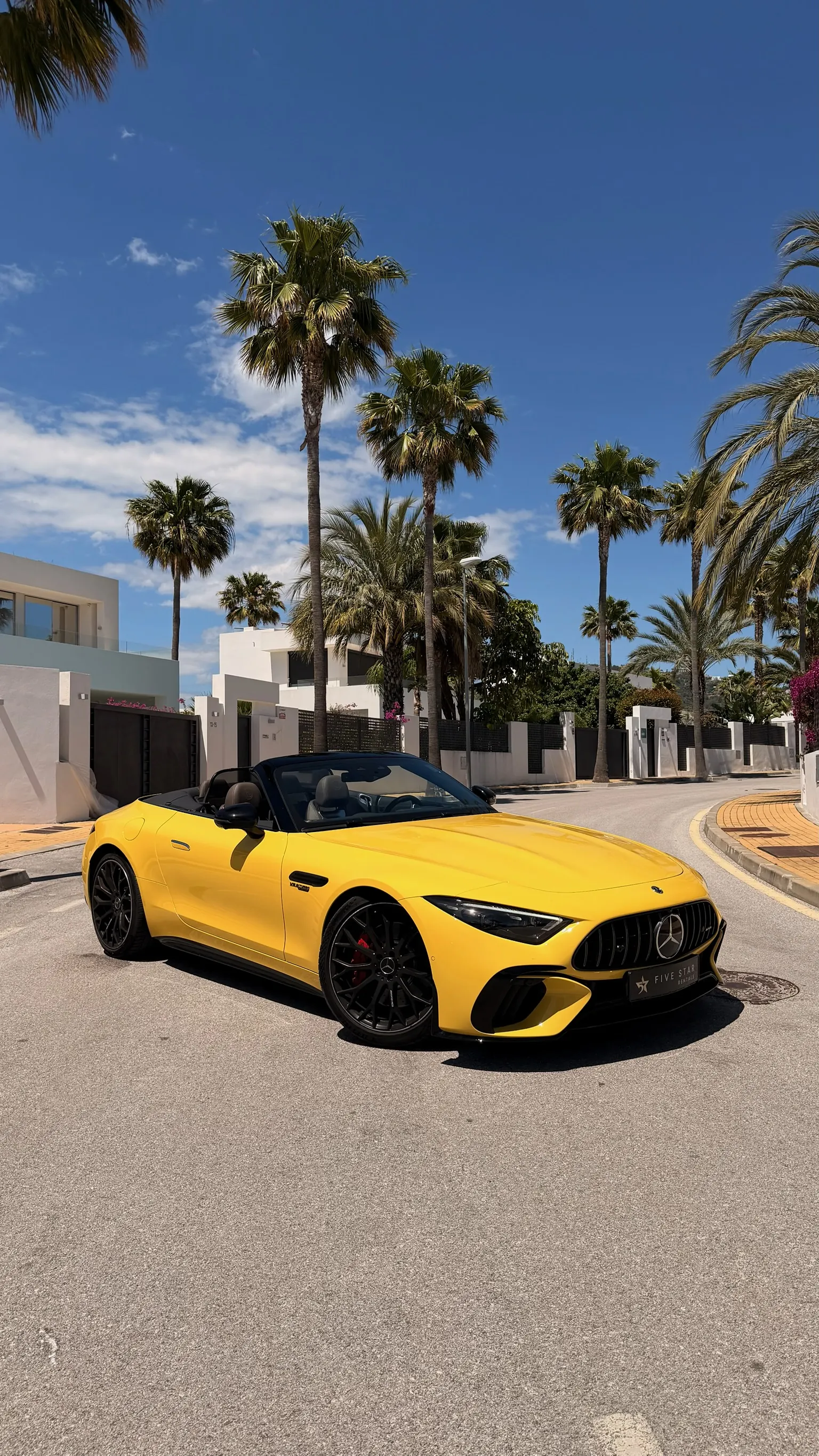 Mercedes-AMG SL 55 4MATIC+ Roadster in Sun Yellow with top down, front three-quarter view with Five Star Rentals plate, vertical chrome grille and Marbella palm trees