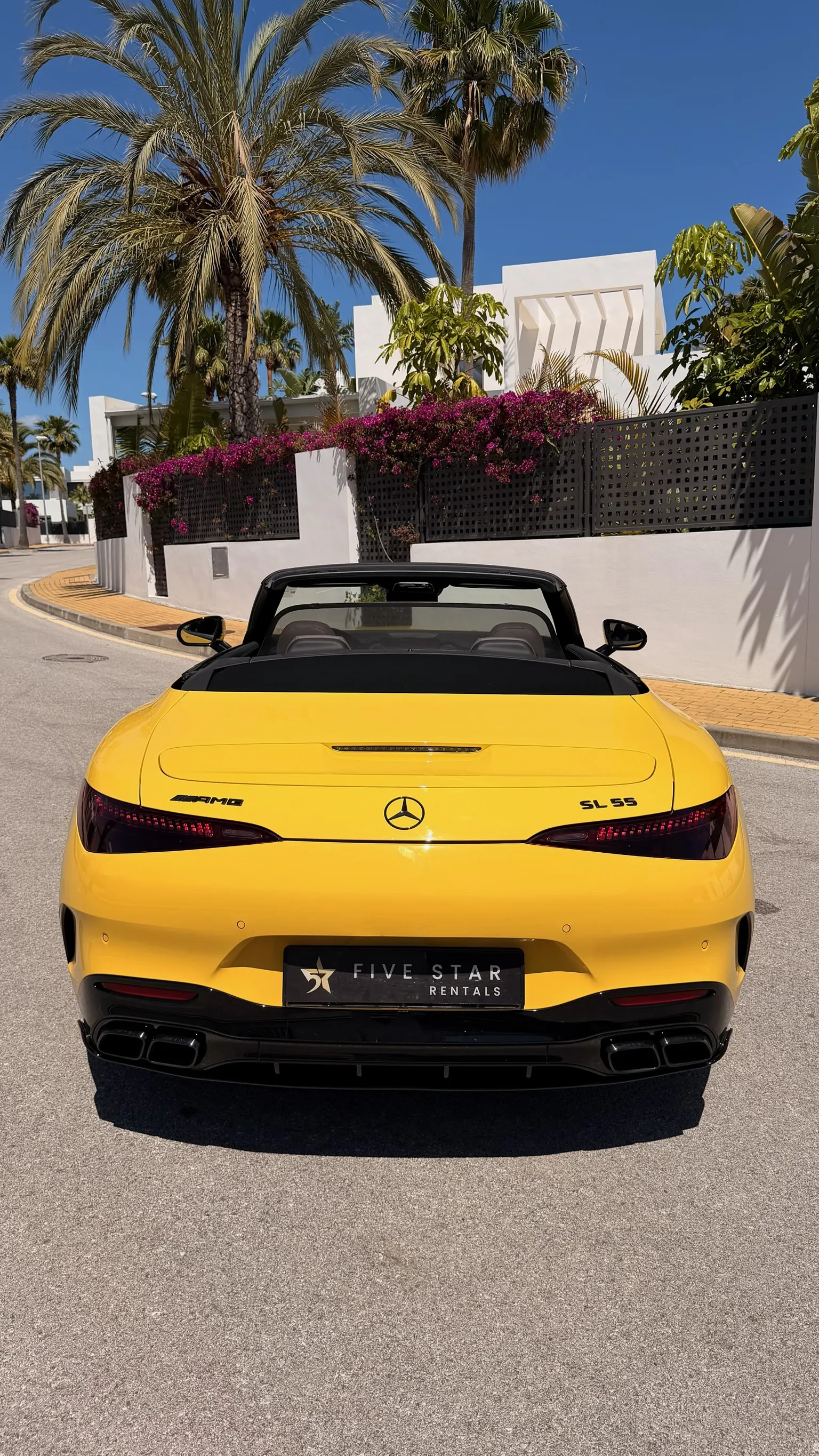 Centered rear view of the Mercedes-AMG SL 55 4MATIC+ in Sun Yellow with Five Star Rentals plate, AMG and SL 55 badges, and dual black exhaust integrated into the diffuser
