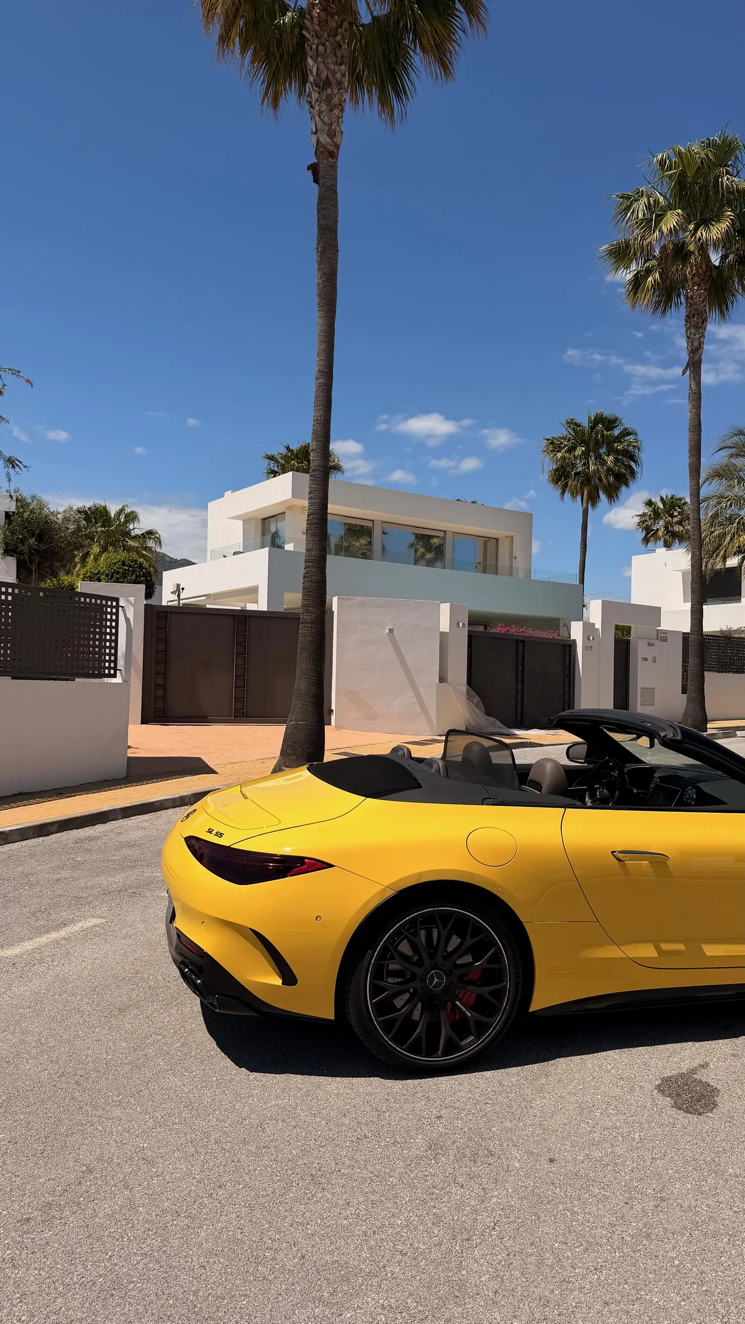 Rear side profile of the Sun Yellow Mercedes-AMG SL 55 with top down, SL 55 trunk badge, 21-inch matte black wheels and red Brembo calipers