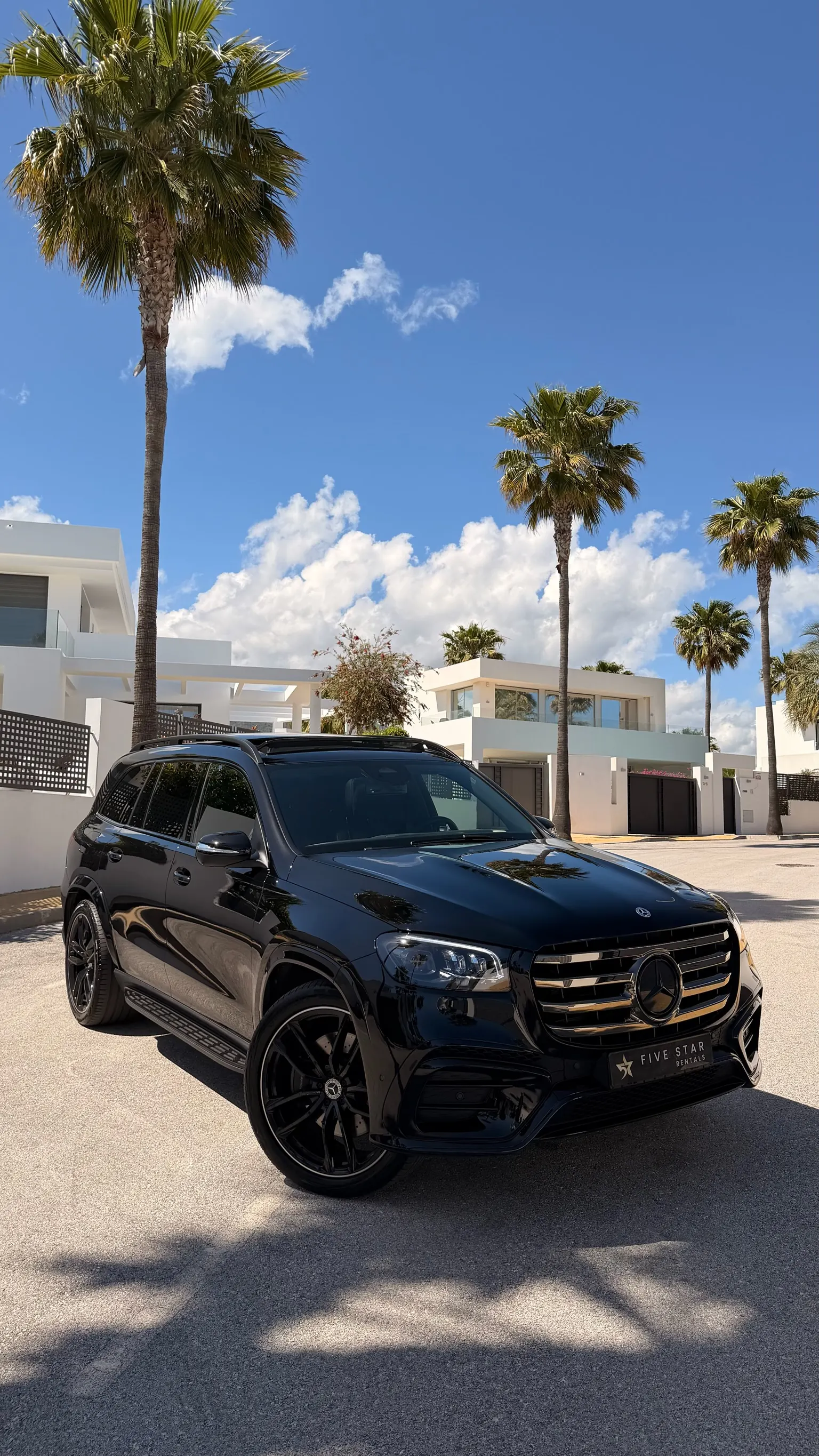 Rear three-quarter view of the Obsidian Black Metallic Mercedes-Benz GLS 580 with Five Star Rentals plate, 22-inch AMG multi-spoke gloss black wheels and roof rails