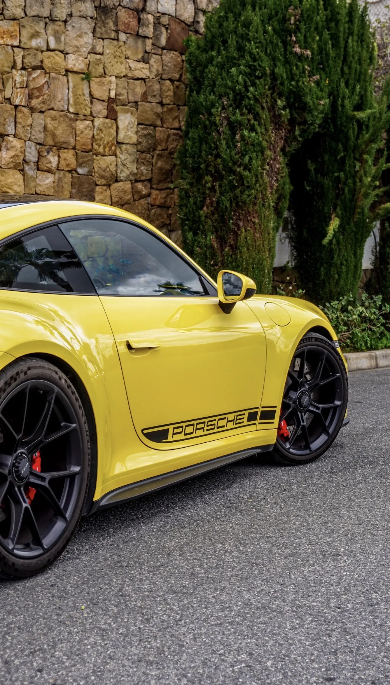 Side profile of the Racing Yellow Porsche 911 GT3 992 with black PORSCHE side decals, matte black forged wheels and red brake calipers