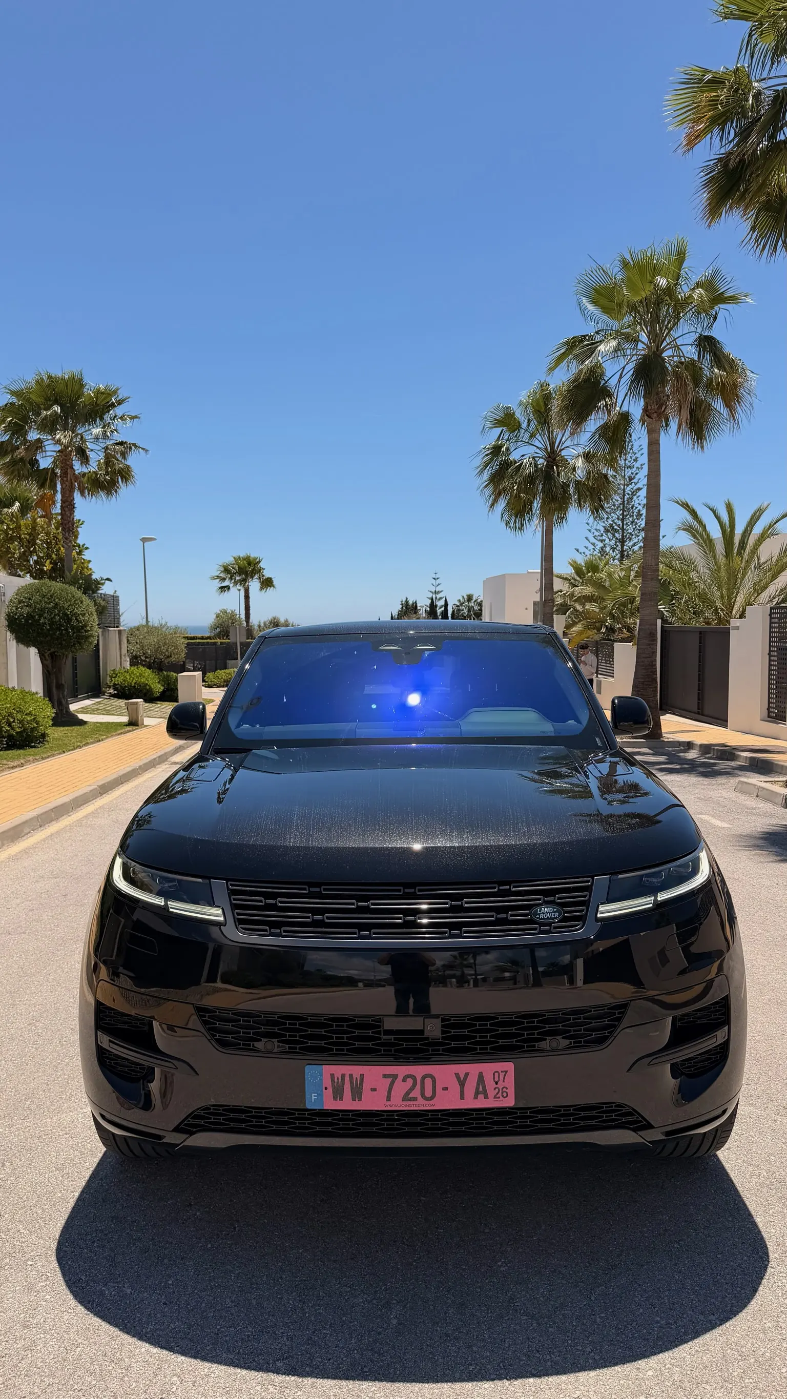 Centered front view of the Santorini Black Range Rover Sport P460e with black grille, LED headlights and sport front bumper under Marbella palm trees